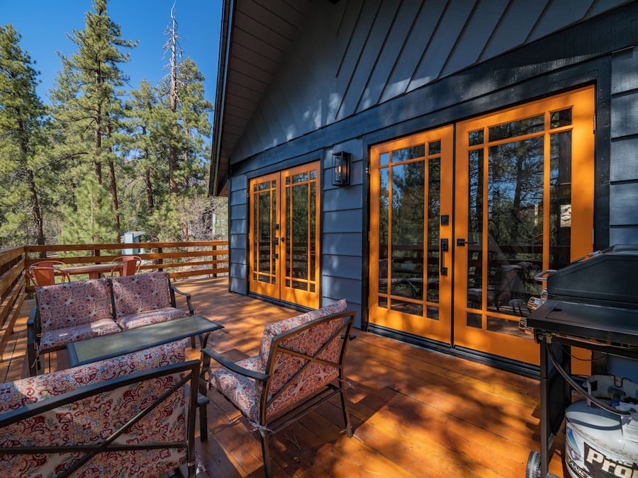 A wooden deck with outdoor furniture, large windows, and a grill.