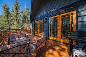Una terraza de madera con mobiliario exterior, ventanas amplias y una parrilla.