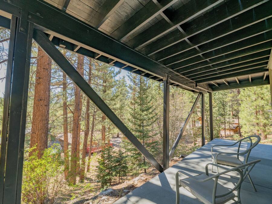 A covered outdoor area with metal beams and a view of a forest. There are two metal chairs on the floor.