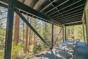 Un espacio al aire libre techado con vigas metálicas y vistas a un bosque. Hay dos sillas metálicas en el suelo.