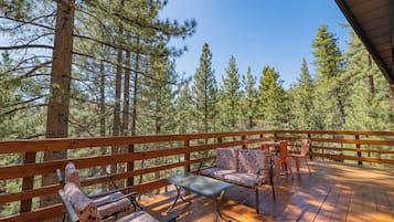 A wooden deck with a table and chairs, surrounded by tall pine trees.