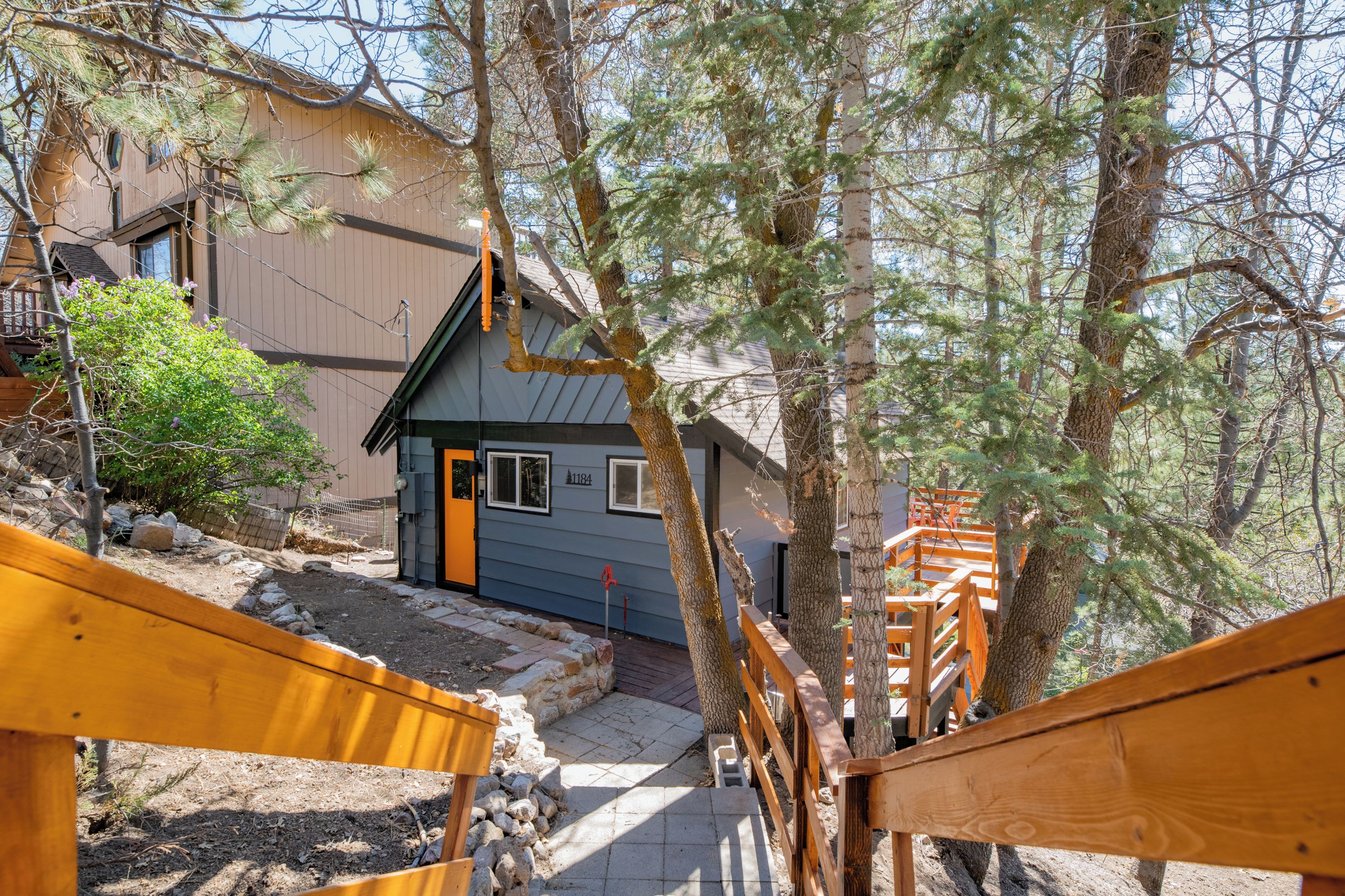 A wooden staircase leading to a house with a blue door, surrounded by trees and a rocky ground.
