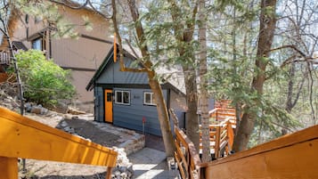 A wooden staircase leading to a house with a blue door, surrounded by trees and a rocky ground.
