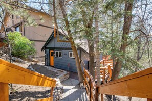 A wooden staircase leading to a house with a blue door, surrounded by trees and a rocky ground. - Forest Escape  (Fawnskin)