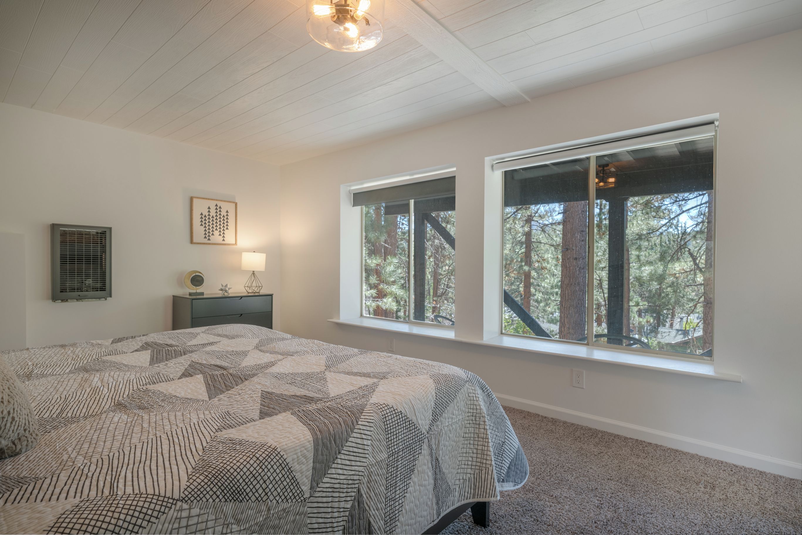 A bedroom with a large bed, two windows, a ceiling fan, and a nightstand with a lamp.