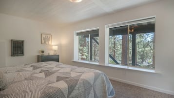 A bedroom with a large bed, two windows, a ceiling fan, and a nightstand with a lamp.