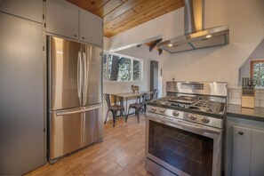 A modern kitchen with stainless steel appliances, a wooden ceiling, and a large window providing natural light. - Forest Escape  (Fawnskin)