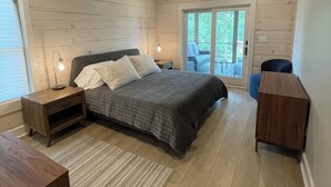 Ett sovrum med en säng, sängbord, ett skrivbord, en stol och en skjutdörr i glas som leder ut till ett utomhusområde.