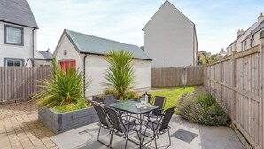Une terrasse avec une table et des chaises, entourée d’une clôture en bois et d’une pelouse.