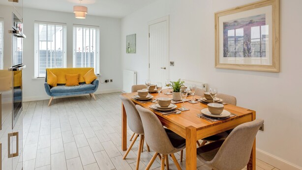 Un coin repas avec une table en bois dressée pour quatre personnes, un canapé bleu et un tableau encadré au mur.