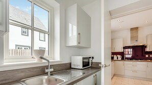 Une cuisine moderne dotée d’un évier en acier inoxydable, de meubles blancs, d’un four à micro-ondes et d’une fenêtre donnant sur une maison.