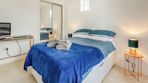 Une chambre à coucher avec un lit, une table de chevet, une lampe, un miroir et un téléviseur posé sur un meuble.