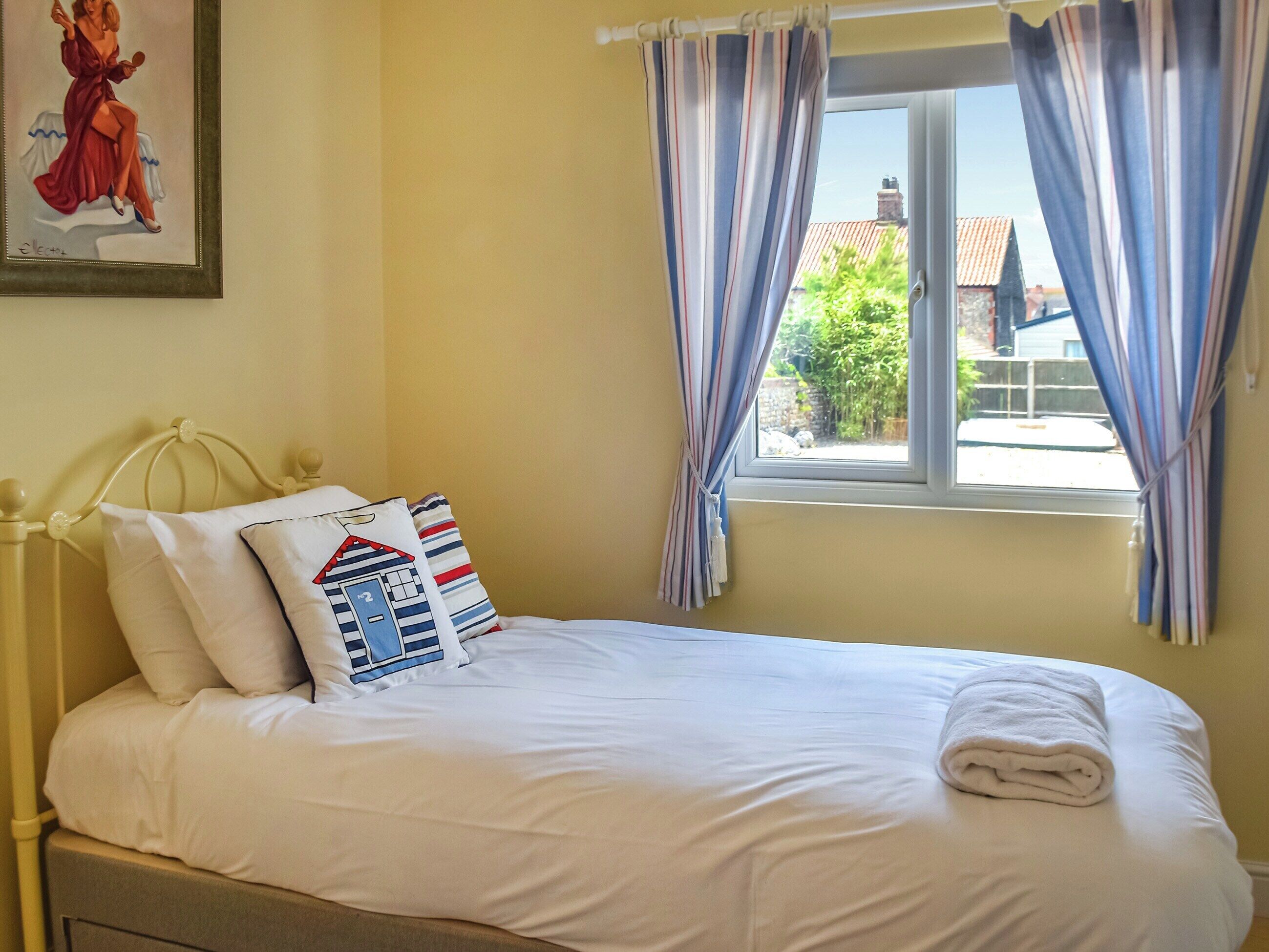 A neatly made bed with white linens and a folded towel, a striped curtain, and a framed picture on the wall.