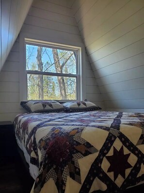 Un dormitorio con un ventanal grande, una cama con colcha y paredes de madera.