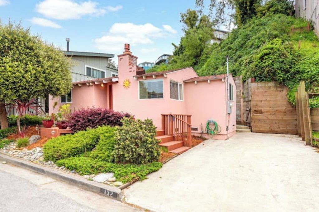 A pink house with a small porch, a chimney, and a garden with various plants.