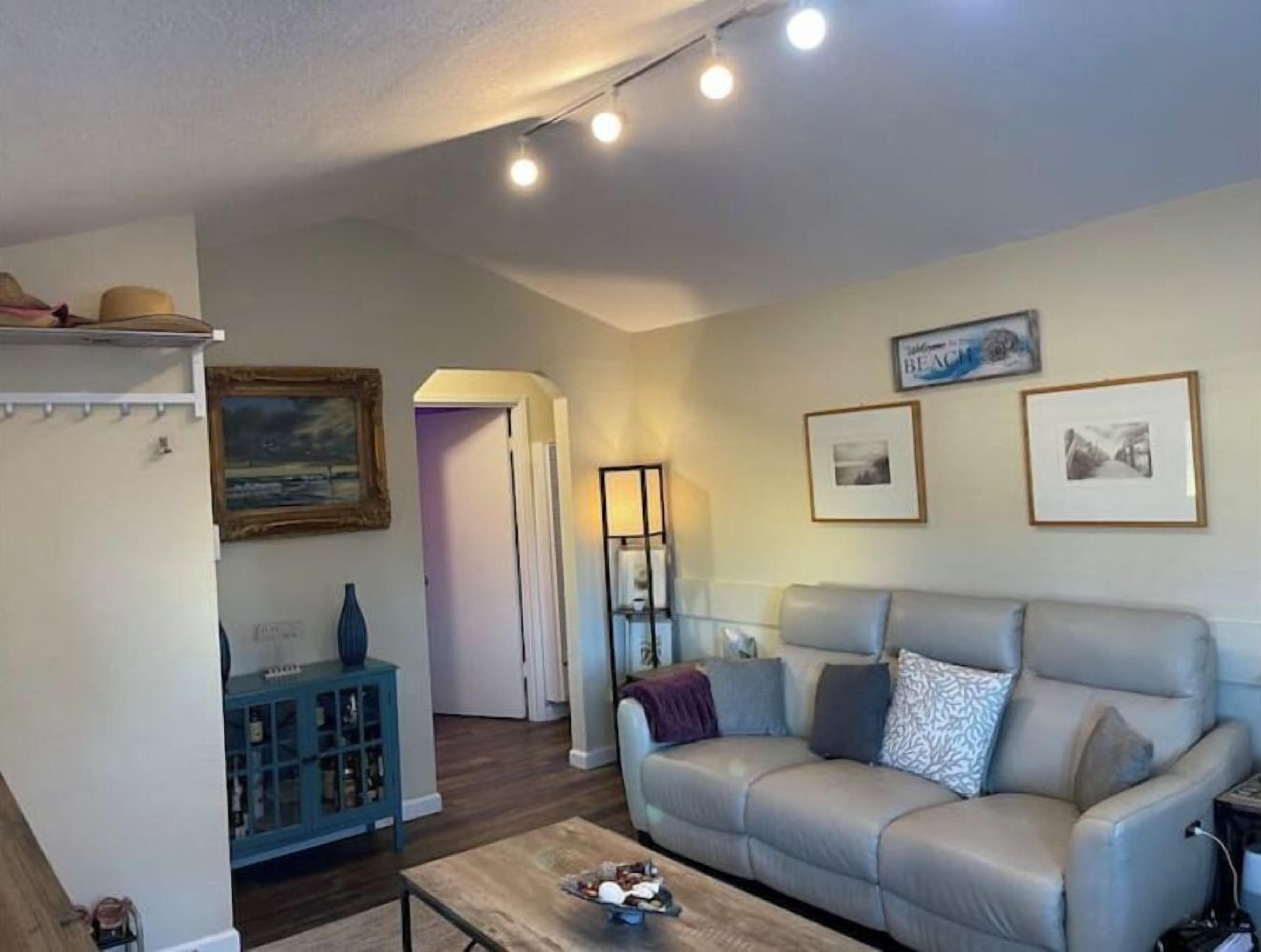 A living room with a grey sofa, a coffee table, and a blue cabinet. There are three framed pictures on the wall and a lamp on a side table.