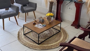 A hotel lobby with a reception desk, grey chairs, a coffee table with decorative items, a fire extinguisher, and a television mounted on the wall. - BOM SOSSEGO POUSADA (Delmiro Gouveia)