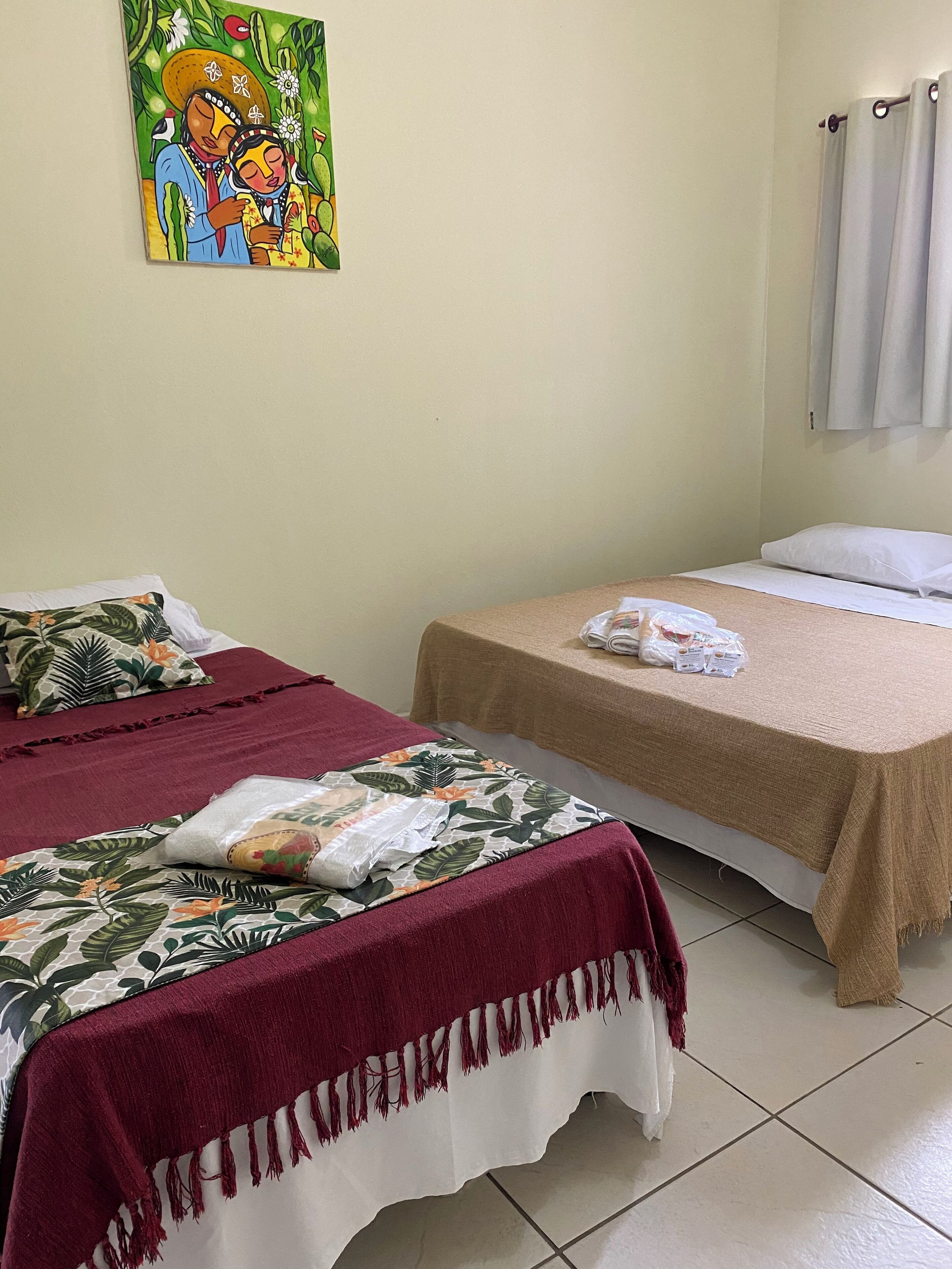 Habitación de hotel con dos camas, cada una con un edredón de diferente color, un cuadro en la pared y una cortina en la ventana.
