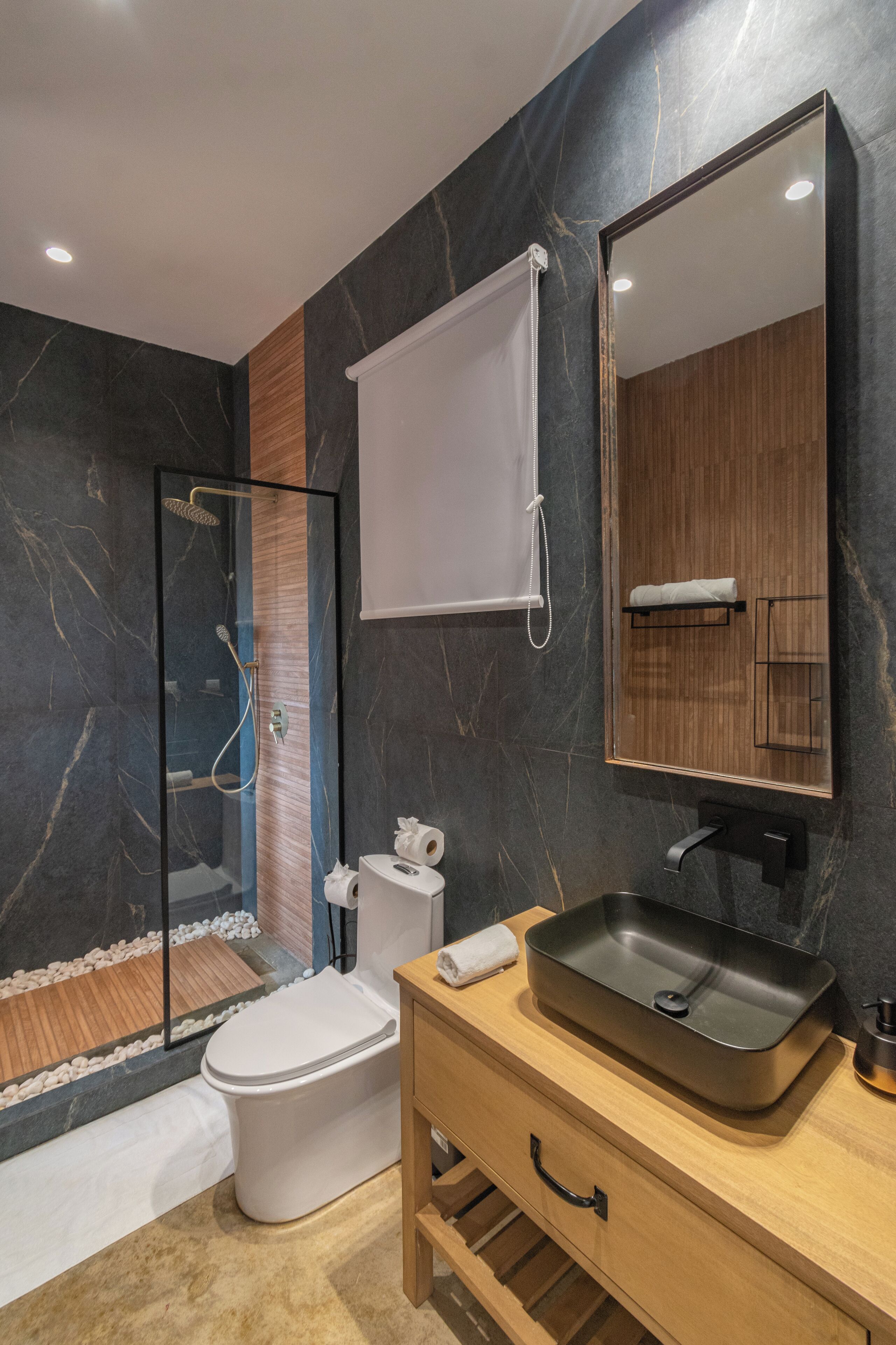 Un baño moderno con ducha de vidrio, inodoro, lavamanos con espejo y tocador de madera.