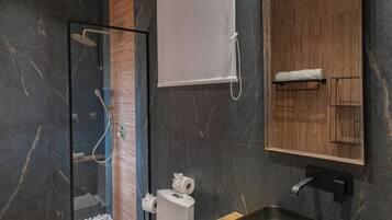 Un baño moderno con ducha de vidrio, inodoro, lavamanos con espejo y tocador de madera.