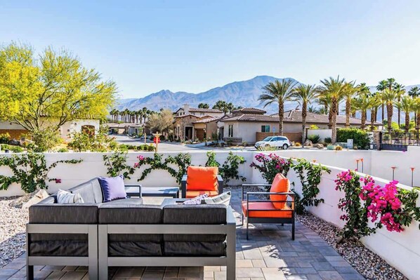 A patio with outdoor furniture, a white wall with climbing plants, and a mountain view in the background.
