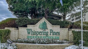 A sign for Whispering Pines Condominiums with a triangular top and a pine tree symbol. - OverlookingCityLightsPigeonForge (Pigeon Forge)