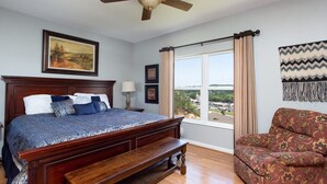 A bedroom with a large bed, a wooden bench, a ceiling fan, a window with curtains, and a view of the outside. - OverlookingCityLightsPigeonForge (Pigeon Forge)