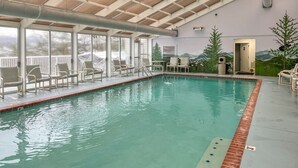 An indoor swimming pool with clear glass walls, lounge chairs, and a view of mountains through the windows. - OverlookingCityLightsPigeonForge (Pigeon Forge)