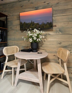 Een houten interieur met een ronde tafel, twee stoelen, een zwarte speaker en een potplant met witte bloemen.