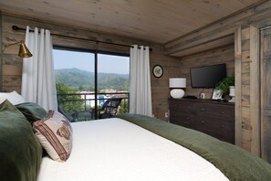 A bedroom with a bed, a dresser, a television, and a view of the outdoors. - Walk2DwTnGatlinburg/MountainView (Gatlinburg)