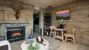 Una sala acogedora con chimenea, paredes de madera, un comedor con sillas y una estantería.