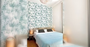 A bedroom with a bed, a nightstand, a lamp, and a wall with a leafy pattern.