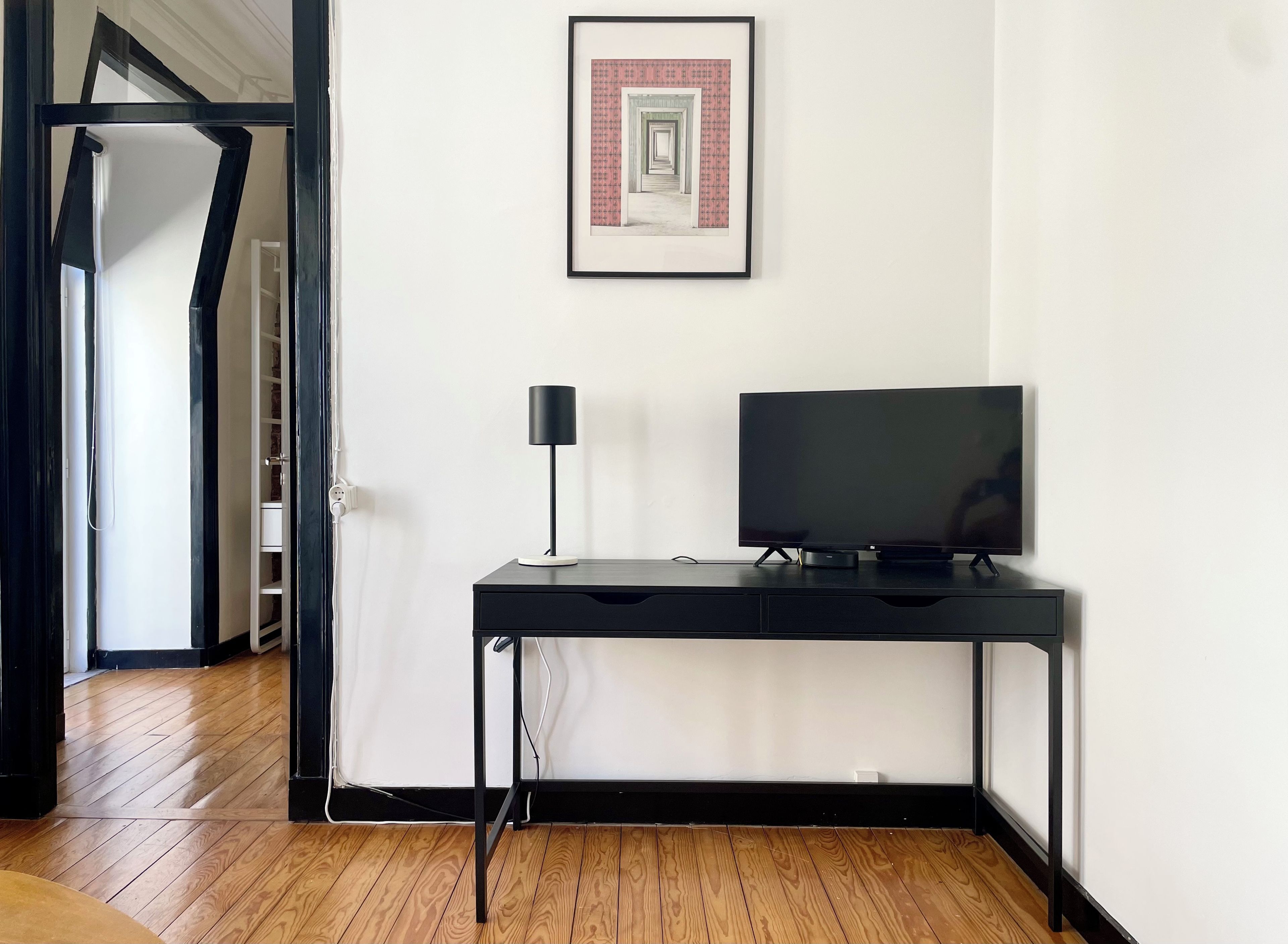 Una habitación con un escritorio negro, un televisor y un cuadro en la pared.