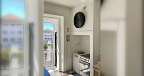 Une petite cuisine équipée d’une cuisinière, d’un évier et d’une fenêtre donnant sur un immeuble.