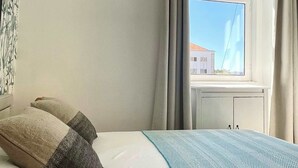 Hotellihuone, jossa on sänky, ikkuna, josta on näkymä rakennuksiin, ja patteri.