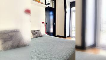 Quarto moderno com cama, mesa de cabeceira, abajur e porta para uma varanda.