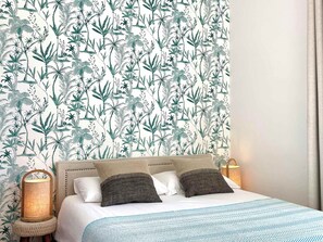 Ein Schlafzimmer mit gestreiftem Wandpapier, einem Bett mit weißer Bettwäsche, zwei Kissen, einer Nachttischlampe und einem kleinen Tisch mit einer Lampe.