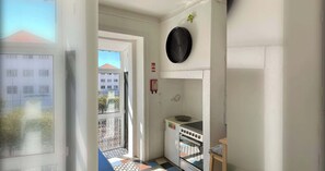 A small kitchen with a stove, a small table, and a window with a view of buildings. - Central Hidden Gem Rustic Modern 2BDR City Flat (Lisboa)
