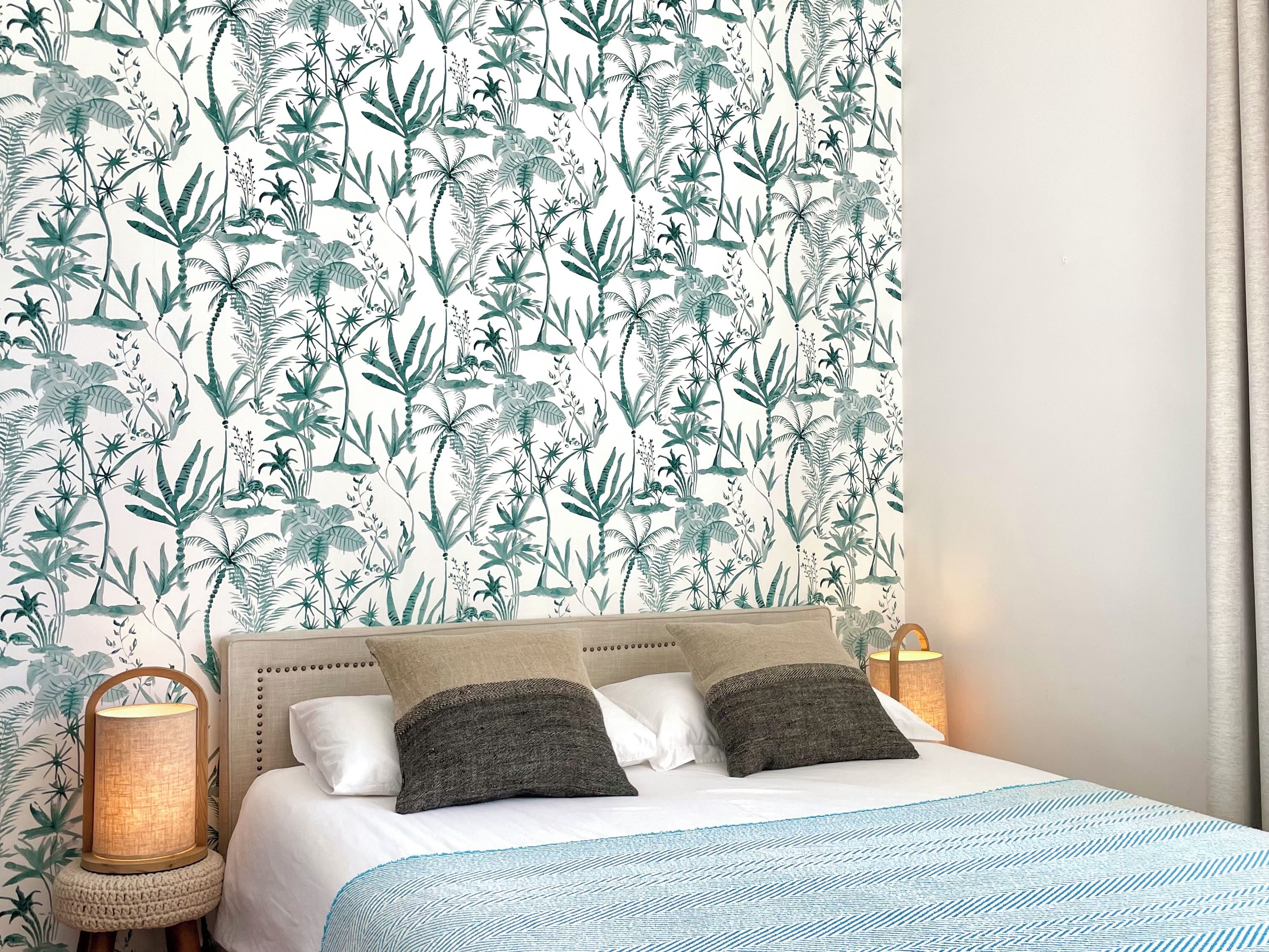 A bedroom with a patterned wallpaper, a bed with white bedding and blue accents, and two bedside lamps.