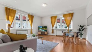 A modern living room with a sofa, coffee table, TV, and dining area with chairs and a table. - Exclusive Apartment in Centre (Bratislava)