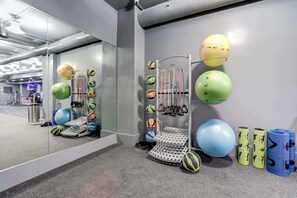 A gym with exercise equipment, including a wall-mounted rack with various balls and a step platform.
