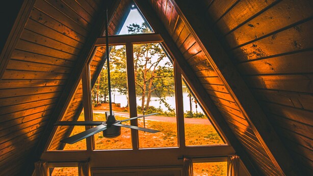 A triangular wooden ceiling with a ceiling fan and a window overlooking a road and trees.