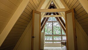 A bedroom with a sloped ceiling, a bed, and a view of the outdoors through a window.