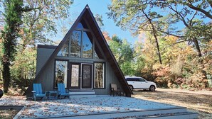 A modern cabin with a triangular roof, large windows, and a deck with outdoor seating.