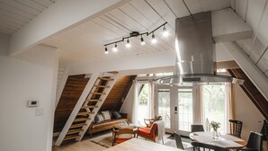 A loft-style room with a wooden staircase, a dining area, and a large window.