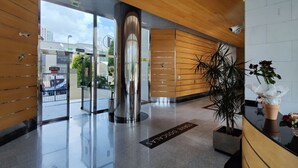 A modern lobby with a glass door entrance, a large metallic column, wooden paneling, and a potted plant. - DOS CALAS sunny apartment (Benidorm)