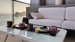 Un balcon avec un canapé blanc, deux plantes en pot et une table avec un plateau en verre.