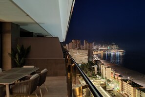 A balcony with a dining area overlooking a cityscape and a beach at night. - SUNSET CLIFFS modern apartment (Benidorm)