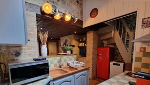 A compact kitchen with a microwave, sink, and red refrigerator. There is a wooden ceiling and a staircase leading to another level. - La Terrasse de Sacha | House with Terrace & Fireplace | 4 Guests (Honfleur)