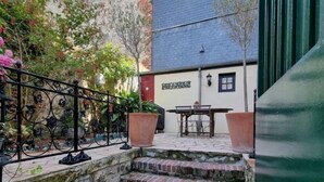 A stone staircase leading to a terrace with a table and chairs, surrounded by greenery and a building with a blue roof. - La Terrasse de Sacha | House with Terrace & Fireplace | 4 Guests (Honfleur)